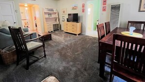 Un salon avec un canapé, une table à manger en bois et des chaises, un téléviseur posé sur un meuble et un sol recouvert d’une moquette.