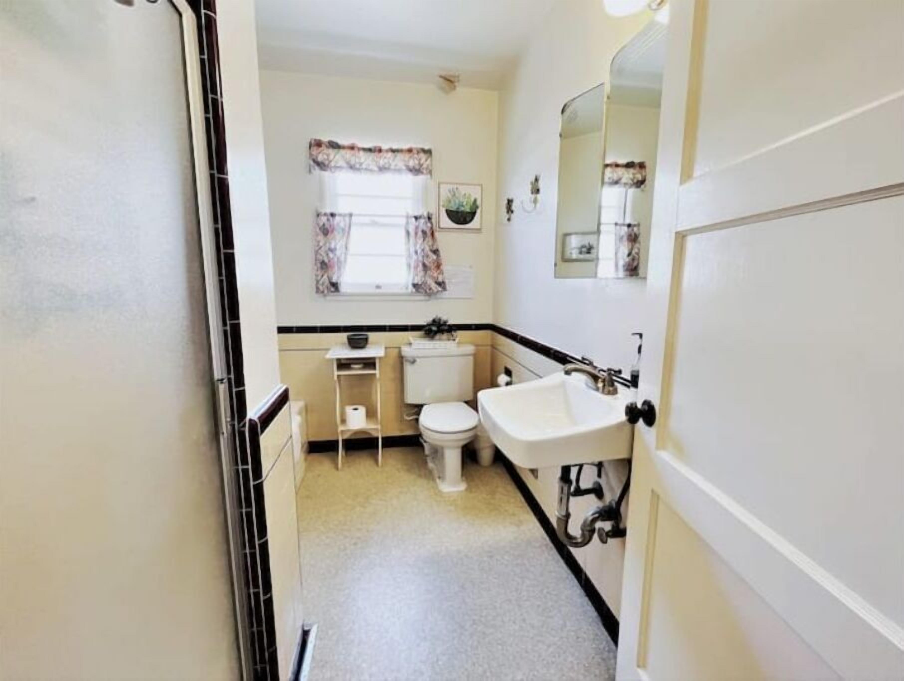 Een kleine badkamer met toilet, wastafel en een klein raam met gordijnen.