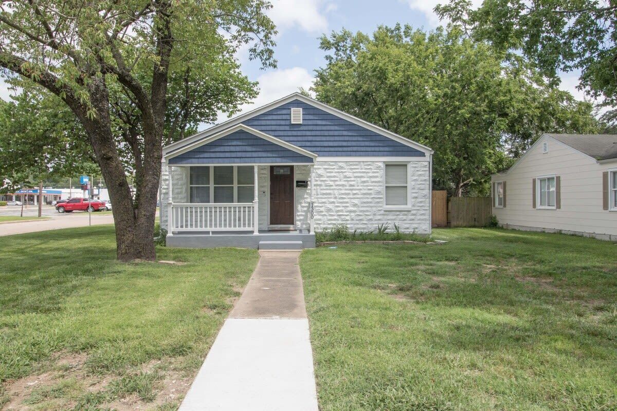 A single-story house with a front porch, a visible garage door, and a tree in the front yard.