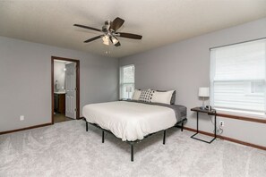 A bedroom with a bed, a ceiling fan, a bedside table, and a window with blinds. - Stadium House - Next to Kernels/Roughriders Arena (Cedar Rapids)