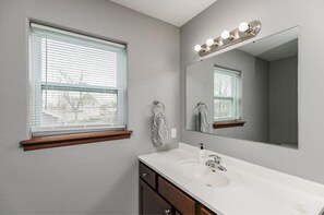 A bathroom with a large mirror, vanity, and window with blinds. - Stadium House - Next to Kernels/Roughriders Arena (Cedar Rapids)