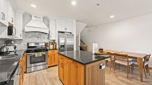 A modern kitchen with stainless steel appliances, wooden cabinets, and a dining area with a wooden table and chairs.