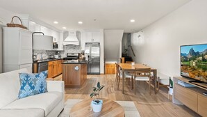A modern kitchen with white cabinets, a central island, and a dining area with a wooden table and chairs.