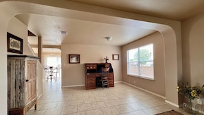 A spacious room with a herringbone tile floor, a wooden desk with drawers, a chair, and a large window providing natural light.