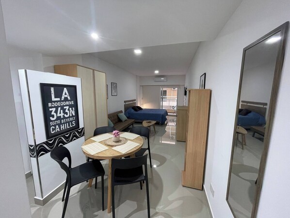 A compact hotel room with a dining area, a bed, and a mirror.