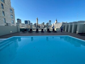A rooftop pool with a city skyline in the background, including a prominent clock tower.
