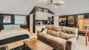 A modern living room with a sofa, a coffee table, and a bed. There is a kitchen area with a microwave and a refrigerator.