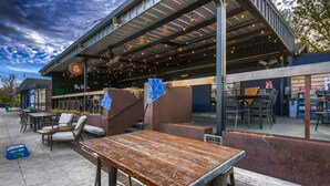 An outdoor seating area with tables and chairs, a covered patio, and a building with a sign.