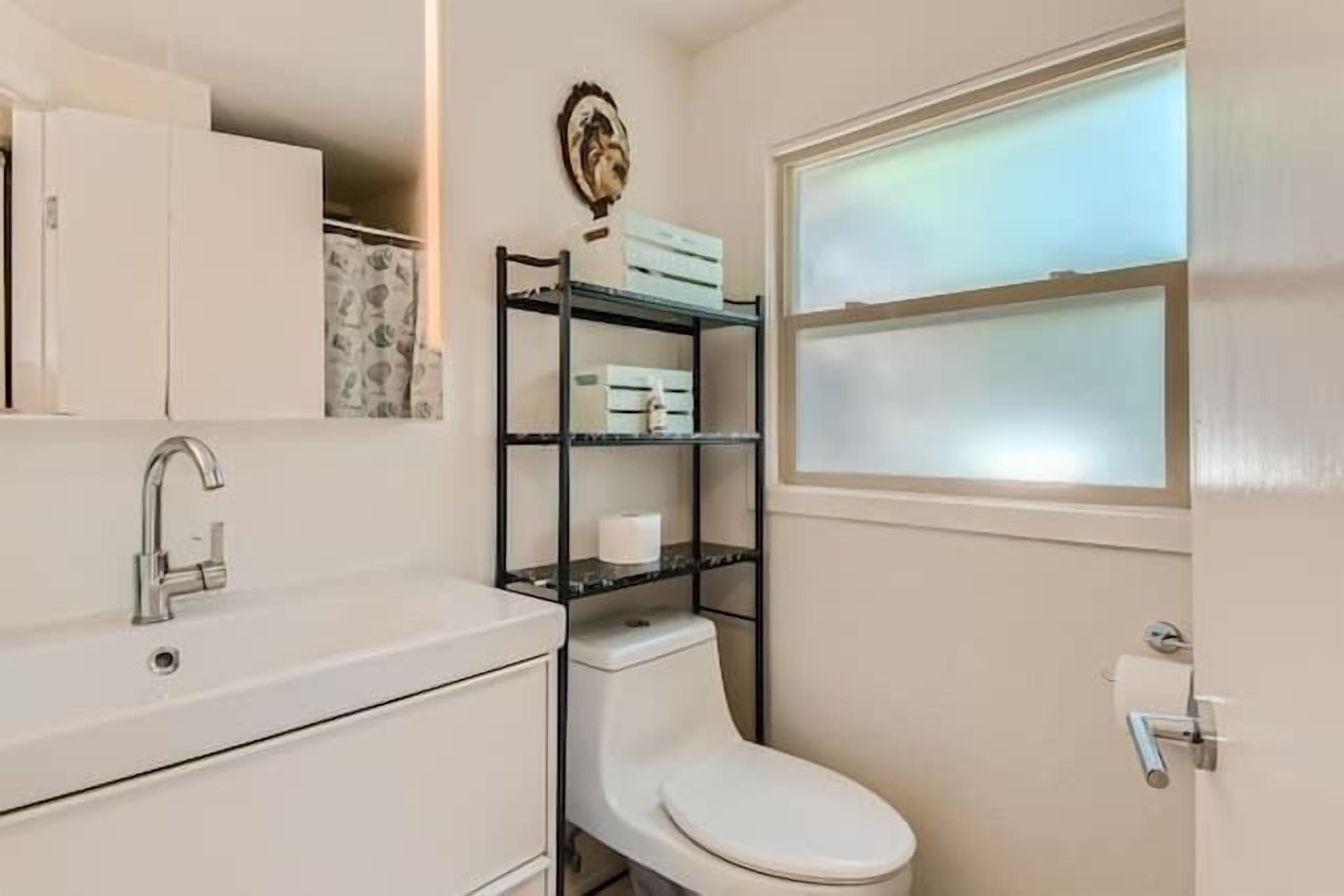 A compact bathroom with a white sink, a toilet, and a window.