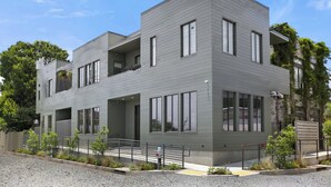 A modern two-story building with large windows, a balcony, and a gravel driveway. - 5BR City Loft - Atop Natural Wine Bar! Steps to Downtown & Magazine!  (New Orleans)