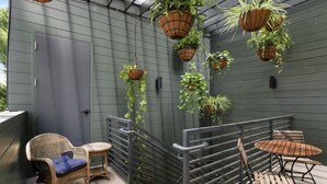A balcony with wicker chairs, a small table, and hanging planters against a green wall. - 5BR City Loft - Atop Natural Wine Bar! Steps to Downtown & Magazine!  (New Orleans)