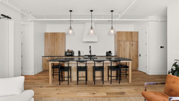 A modern kitchen with a central island, bar stools, pendant lighting, and wooden cabinets. - 5BR City Loft - Atop Natural Wine Bar! Steps to Downtown & Magazine!  (New Orleans)