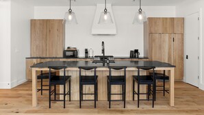 A modern kitchen with a central island, black bar stools, pendant lighting, and wooden cabinetry. - 5BR City Loft - Atop Natural Wine Bar! Steps to Downtown & Magazine!  (New Orleans)