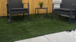 An outdoor seating area with two wicker chairs and a small table with a potted plant, set against a wooden fence and a house. - Cozy Private Entire Studio Suite Independent Guest Entrance (Jacksonville)