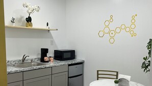 A modern kitchen with grey cabinets, a stainless steel dishwasher, a microwave, and a sink. There's a white marble table with chairs and a small potted cactus. - Cozy Private Entire Studio Suite Independent Guest Entrance (Jacksonville)