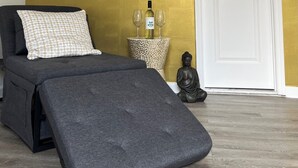 A room with a sofa, a small table with a bottle and glasses, a Buddha statue, and a white door. - Cozy Private Entire Studio Suite Independent Guest Entrance (Jacksonville)