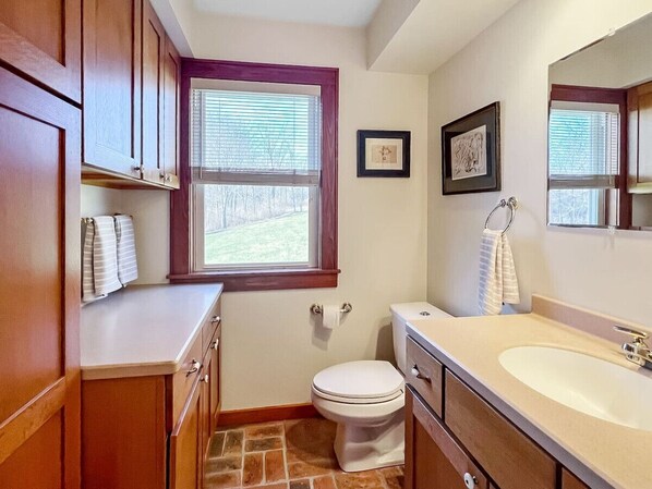 A bathroom with wooden cabinets, a white toilet, a beige sink, and a window with blinds.