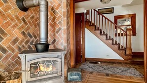 Ein Kaminofen in einem Raum mit Backsteinwand, einer Holztreppe und einem gemusterten Teppich.