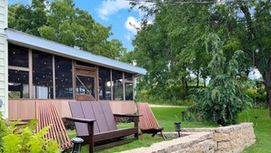 Ein modernes Haus mit Terrasse, zwei braune Adirondack-Stühle und einer Steinmauer.