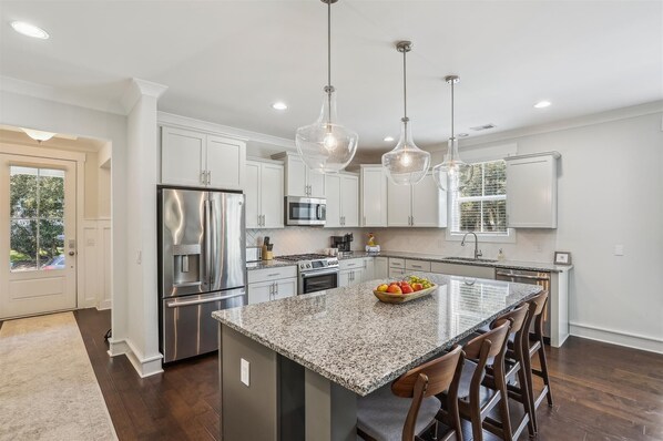 A modern kitchen with white cabinets, stainless steel appliances, a granite countertop, and pendant lighting. - 1 Azalea @ Folly Field Beach | Free Heated Pool | Walk to Beach | EV-charger (Hilton Head Island)