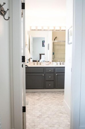 Enter a stylish hallway leading to a bathroom with a large mirror, sink, and dark grey cabinets.