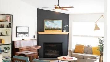 Cozy living room with a fireplace, sofa, and piano, surrounded by a collection of books and decorative items.