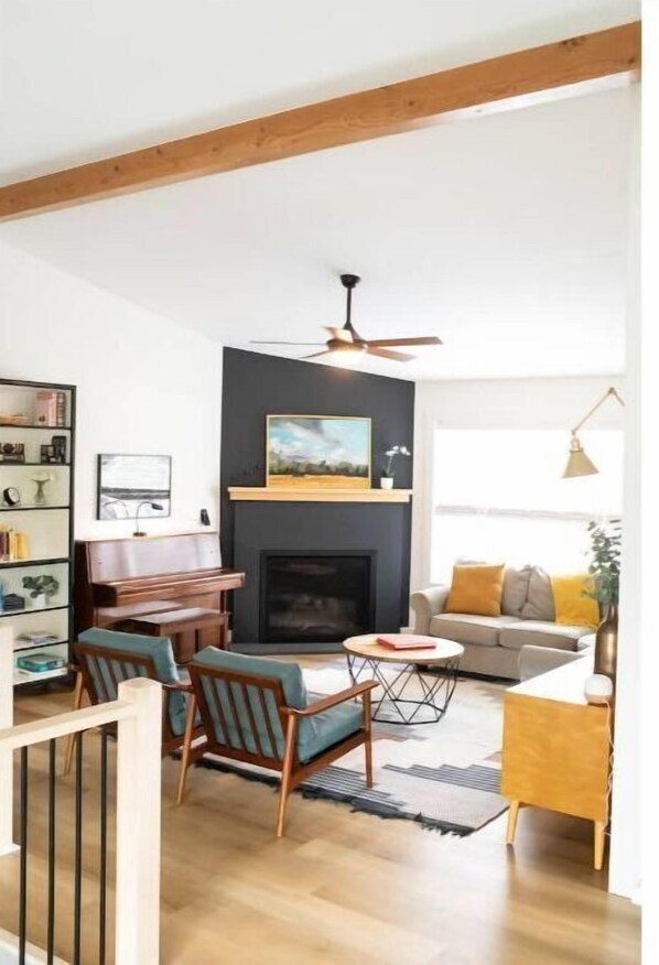 Cozy living room with a fireplace, sofa, and piano, surrounded by a collection of books and decorative items.