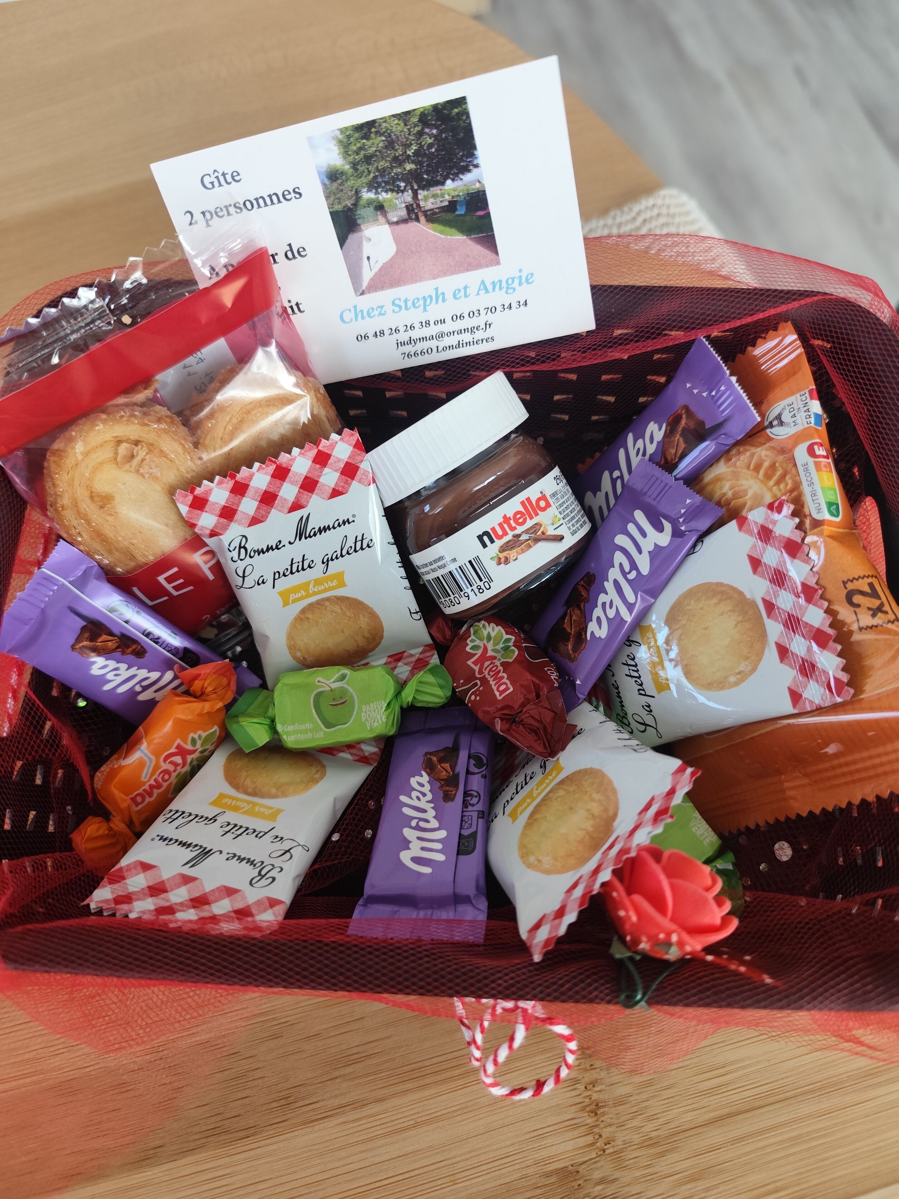 A basket filled with various packaged snacks and a card with contact information.