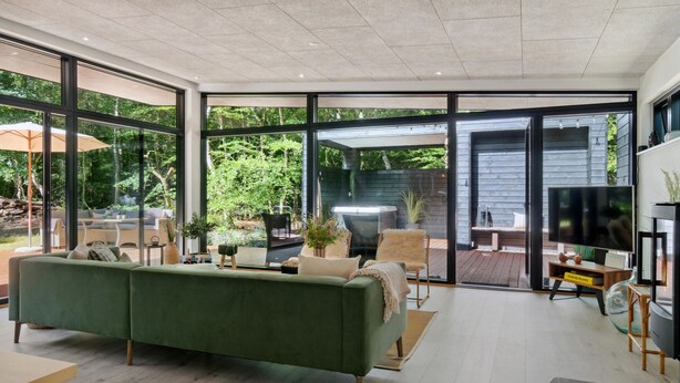 A modern living room with a green sofa, a TV, and a large window overlooking a garden. - Beautiful home in Frederiksværk (Frederiksværk)