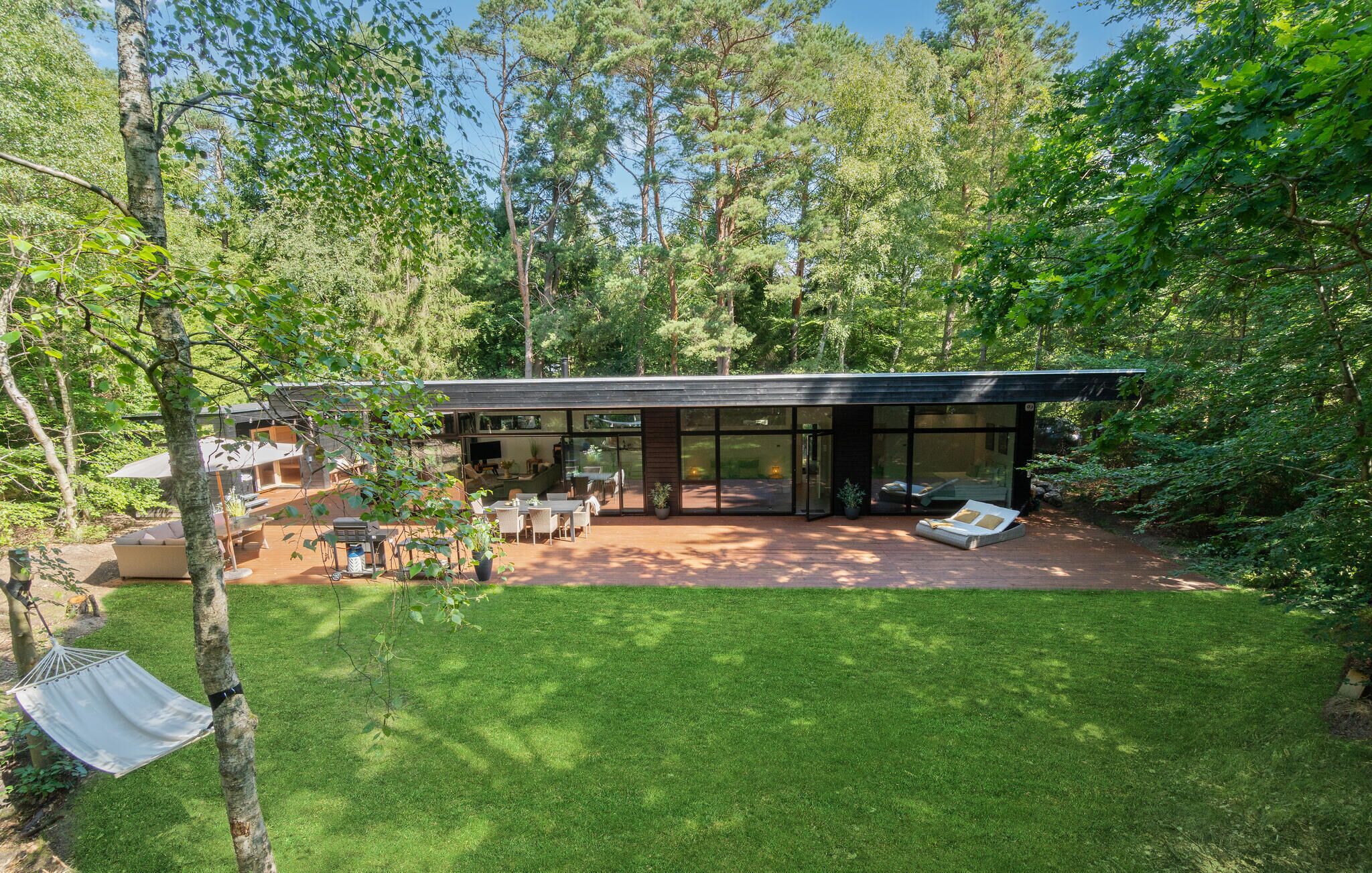 A modern house with a large glass facade, a patio with outdoor furniture, and a well-maintained lawn.