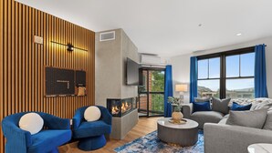 A modern living room with a fireplace, blue and grey sofas, a flat-screen TV, and a large window with curtains. - Steps to Keystone Gondola - River Run Village Condo w/ Hot Tubs (Keystone)