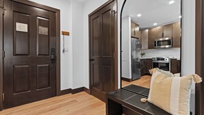 Un interno moderno con pavimento in legno, porte marrone scuro, una panca con cuscini e un angolo cottura con elettrodomestici in acciaio inossidabile.