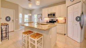 A spacious kitchen with white cabinets, a granite countertop, and a stainless steel refrigerator.