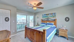 A bedroom with a wooden bed, a ceiling fan, a view of the outside balcony, and a painting on the wall.