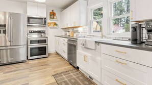A modern kitchen with stainless steel appliances, white cabinetry, and a large window providing natural light. - Camas Lakehouse With Private Hot Tub (Camas)