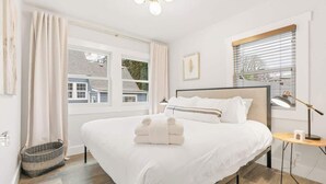 A neatly made bed with white linens and a small bedside table with a lamp. - Camas Lakehouse With Private Hot Tub (Camas)