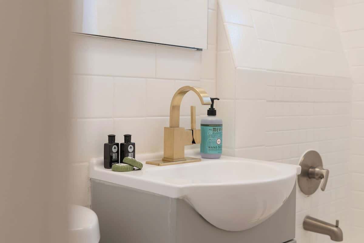 Un bagno con un lavandino bianco, un rubinetto dorato e un erogatore di sapone. Sul lavandino ci sono due flaconi di sapone e un asciugamano verde.