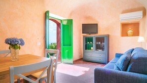 A cozy room with a wooden dining table, a blue sofa, a green cabinet with glass doors, and a TV mounted above it. - Lunarosa, scenic country cottage in Montargano. (Mascali)