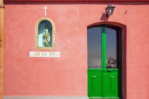 A building facade with a pink wall, a green door, and a religious statue above the door. - Lunarosa, scenic country cottage in Montargano. (Mascali)