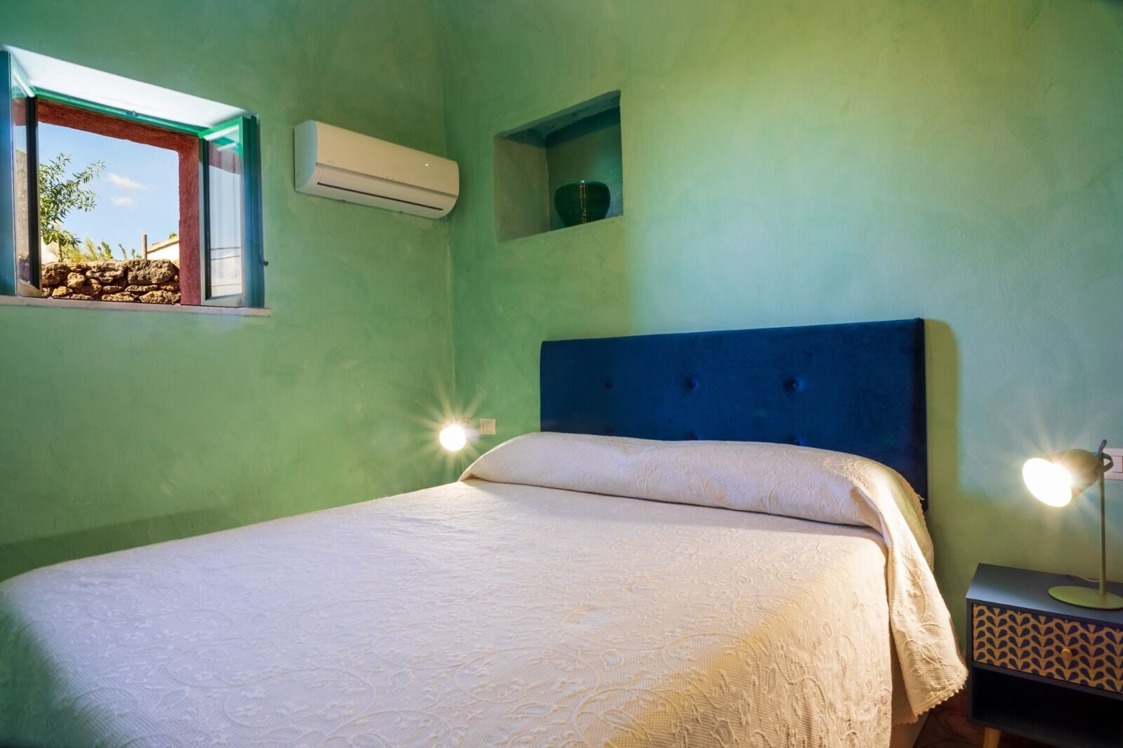 Um quarto com cama, janela, ar condicionado e luminária de cabeceira.