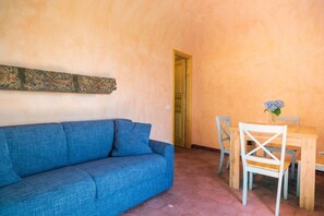 A cozy room with a blue sofa, a wooden dining table with two chairs, and a door leading to another room. - Lunarosa, scenic country cottage in Montargano. (Mascali)