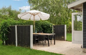 Un patio al aire libre con una mesa, sillas, un paraguas blanco y una valla de madera.