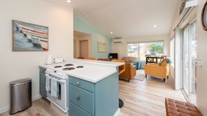 Une cuisine moderne dotée d’un îlot central, un coin repas avec une table et des chaises, et un salon avec un canapé et des fauteuils.