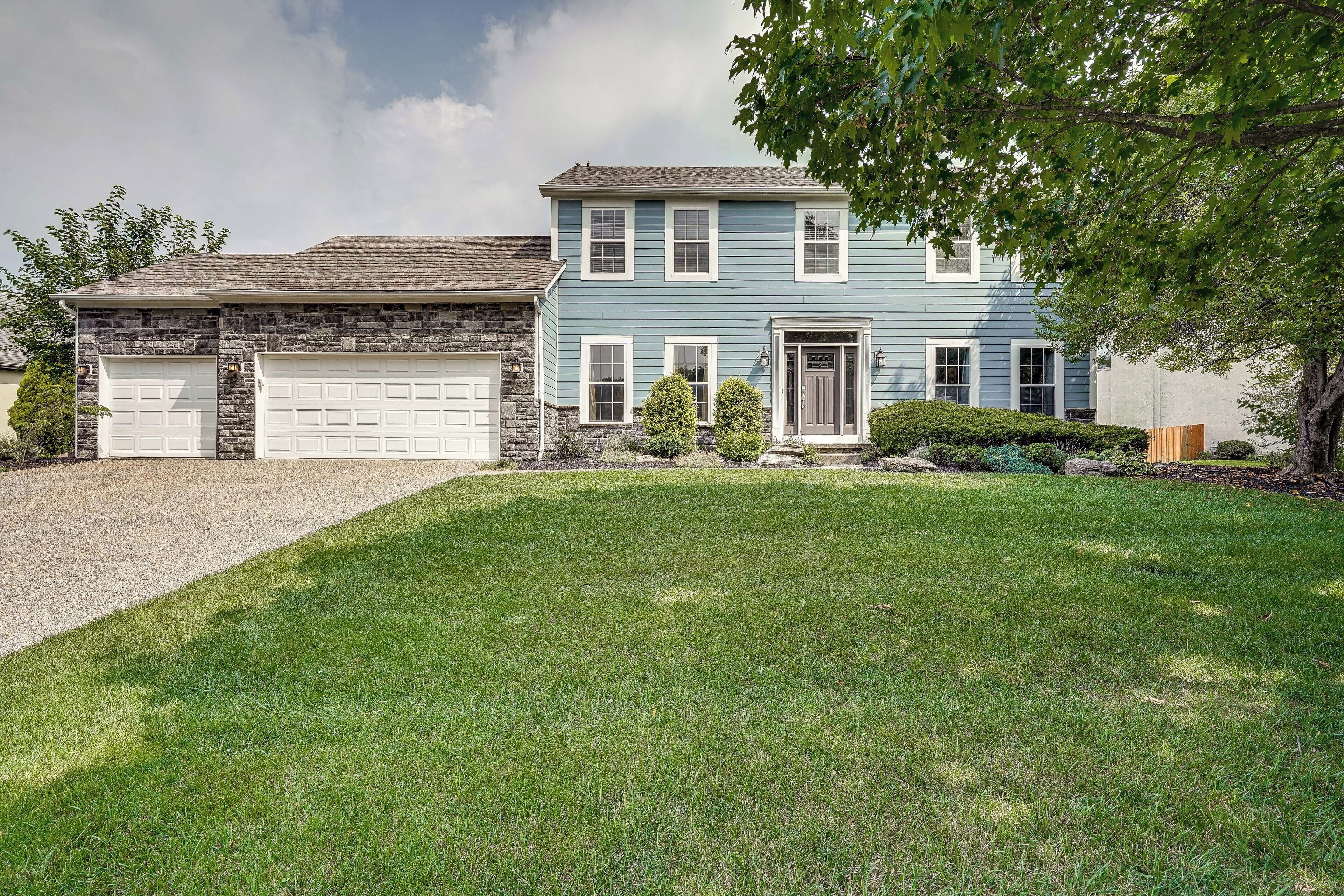 A two-story house with a garage, a well-maintained lawn, and a tree in the front yard.