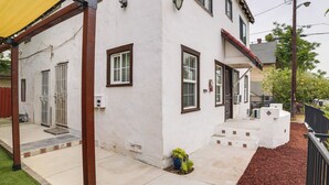 Un edificio blanco con detalles marrones, un porche cubierto y un pequeño jardín con mantillo y una planta en maceta.