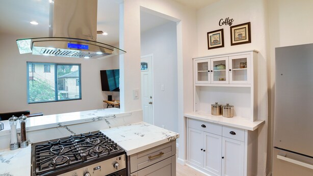 Una cocina moderna con estufa a gas, armarios blancos y horno empotrado. Cuenta con dispensador de agua y una decoración de pared con motivos de café.