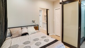 Un dormitorio con cama, mesita de noche, lámpara de pared y puerta corredera que da a un baño.