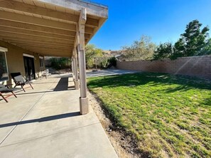 Relax in the serene backyard with a covered patio, lounge chairs, and a lush lawn.