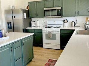 Kitchen features a stainless steel refrigerator, microwave, gas stove, and sink, set against a neutral backdrop of painted cabinets and light-colored wood flooring.