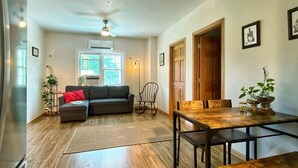 A spacious living area with a wooden floor, a sofa, a dining table with chairs, and a ceiling fan.